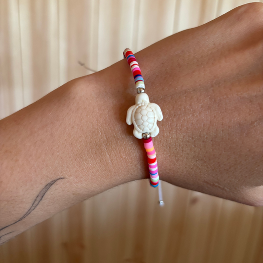 Colourful beaded bracelet with a turtle charm on the wrist against a neutral background